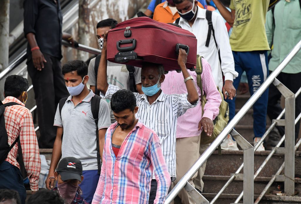 Migrant workers from other states arrive at the Anand Vihar bus terminal, in New Delhi on August 18, 2020. - India's official coronavirus death soared past 50,000 on August 17 as the pandemic rages through smaller cities and rural areas where health care is feeble and stigmatisation rife.