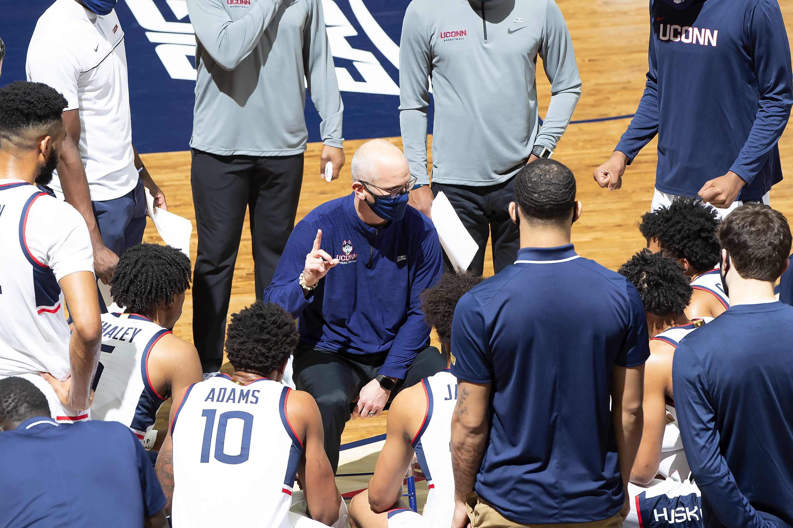 Coach Hurley in a mask surrounding by players in a gameday huddle