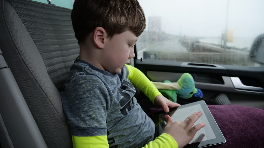 A young boy in a car plays with a tablet computer.