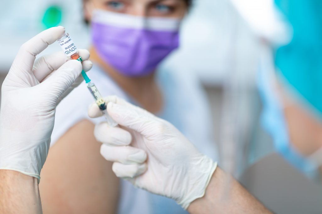 Doctor's hands in surgical gloves preparing COVID-19 vaccine for female patient.