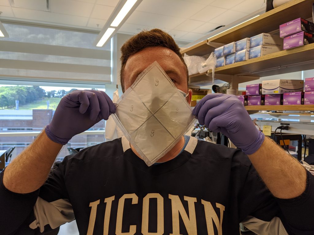 A man in a UConn sweatshirt holds up the biodegradable facemask invented by UConn engineer Thanh Nguyen.