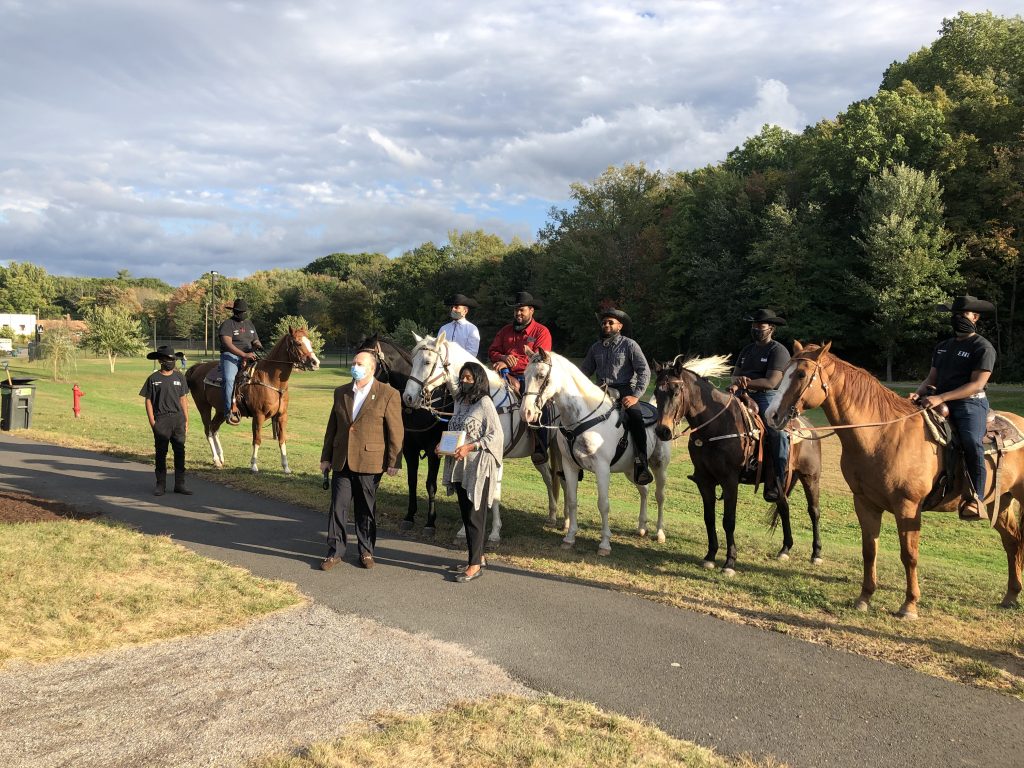 The members of Ebony Horsewomen Inc.'s Junior Mounted Patrol in Keney Park, receiving a Connecticut Greenways award in October 2022, with Ebony Horsewomen founder and CEO Patricia "Pat" Kelly standing in front, with Bruce Donald of the Connecticut Greenways Council
