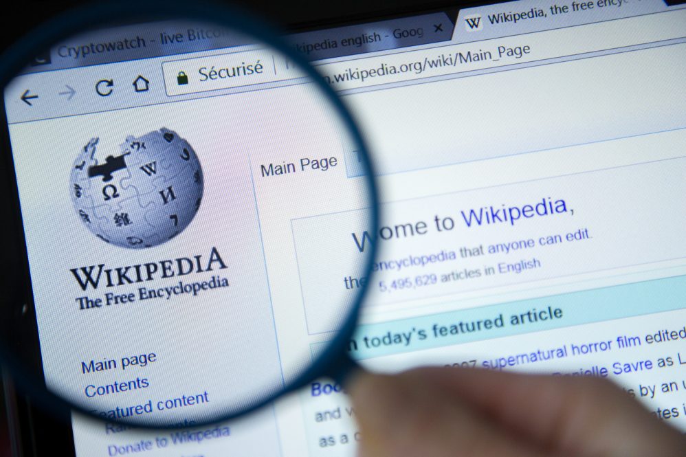 Paris, France - October 19, 2017 : Wikipedia homepage on the computer screen under magnifying glass. Wikipedia is a free Internet encyclopedia.