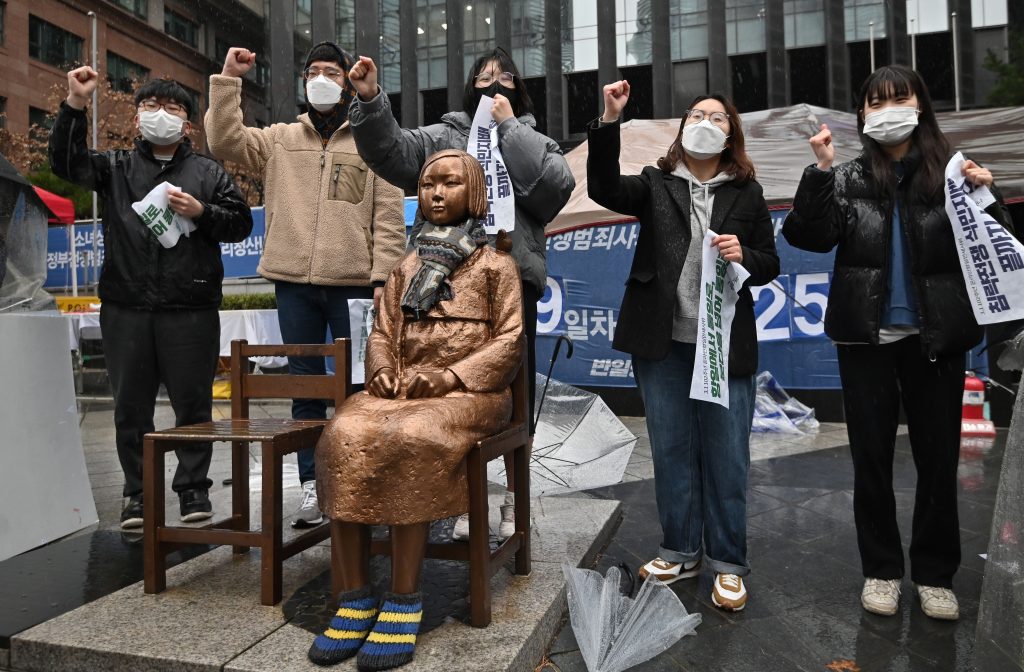 South Korean protesters stand beside a statue of a teenage girl symbolizing "comfort women," who were sex slaves for Japanese soldiers during World War II, near the Japanese embassy in Seoul on March 1, 2021, the 102nd anniversary of the Independence Movement Day against the 1910-1945 Japanese colonial rule.