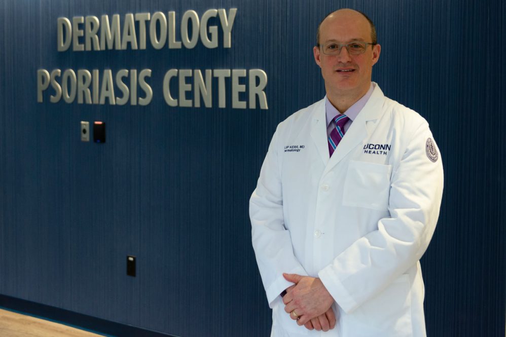 Dr. Philip Kerr in white coat, psoriasis center sign in background