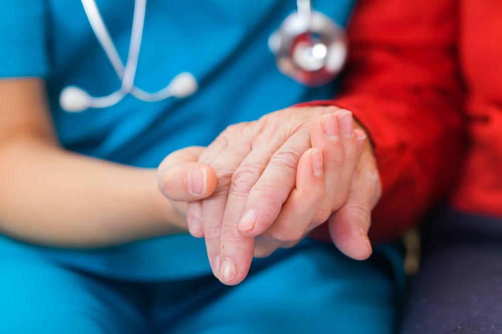 A nurse holds the hand of an elderly patient.