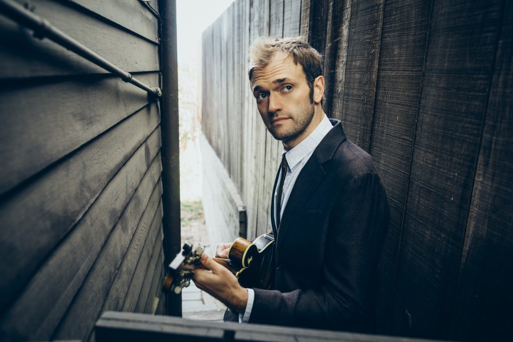 Chris Thile holding a mandolin in a posed photograph. He will perform virtually for a UConn audience on April 17.