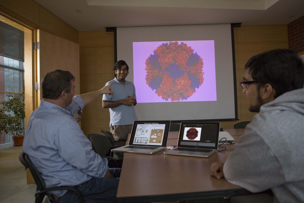 "Dr. Eric May (left) discusses virus research with students Prakhar Bansal (standing) and Shaan Kamal (right).