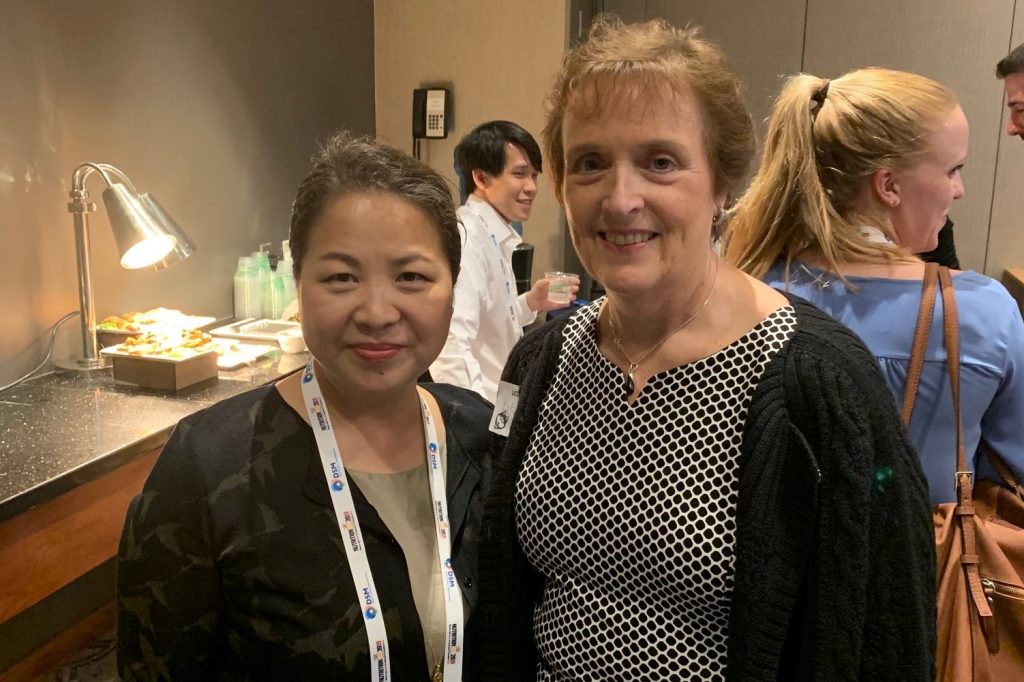 An Asian woman stands next to a Caucasian woman at a networking event