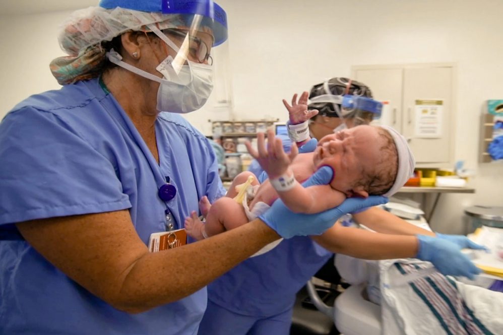 Nurse Lina Godfrey, wearing personal protective equipment, holding a newborn