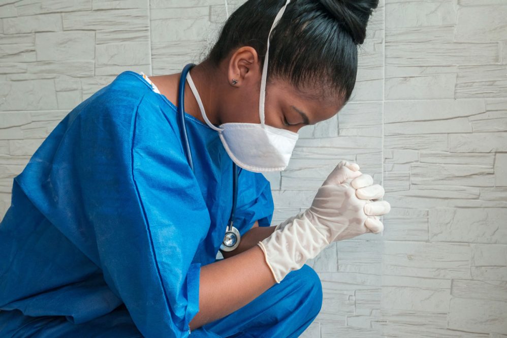 nurse in scrubs with mask and gloves in prayer or reflection