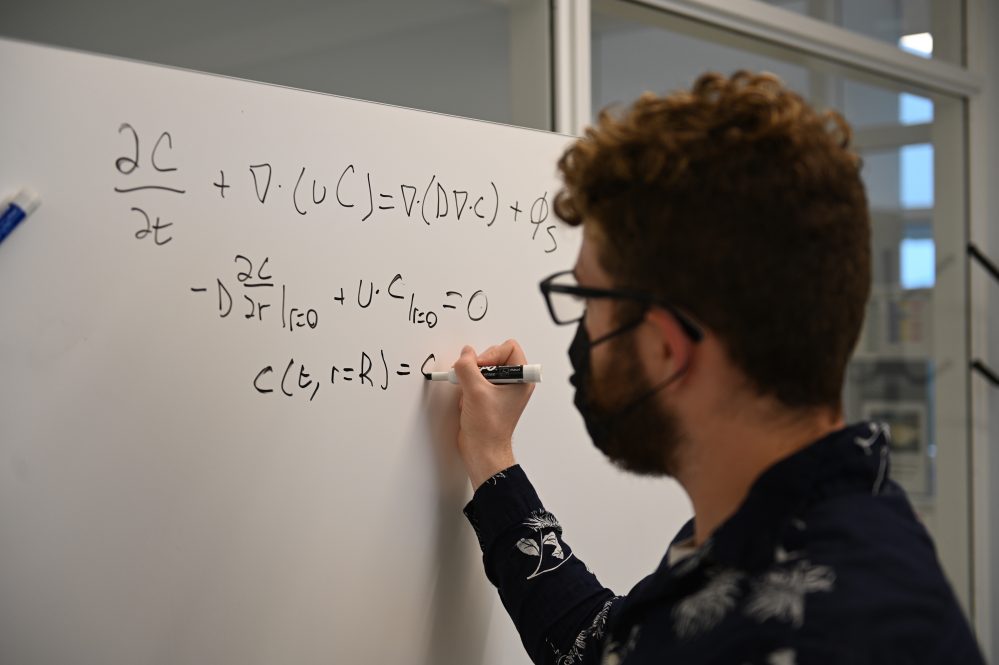 student working on an equation at a whiteboard