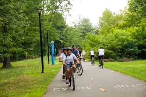 People riding bicycles on a paved trail through a wooded area. Connecticut has more than 2,000 miles of trails.