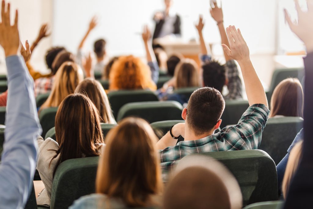 Back view of college students raising their arms on a class at lecture hall.