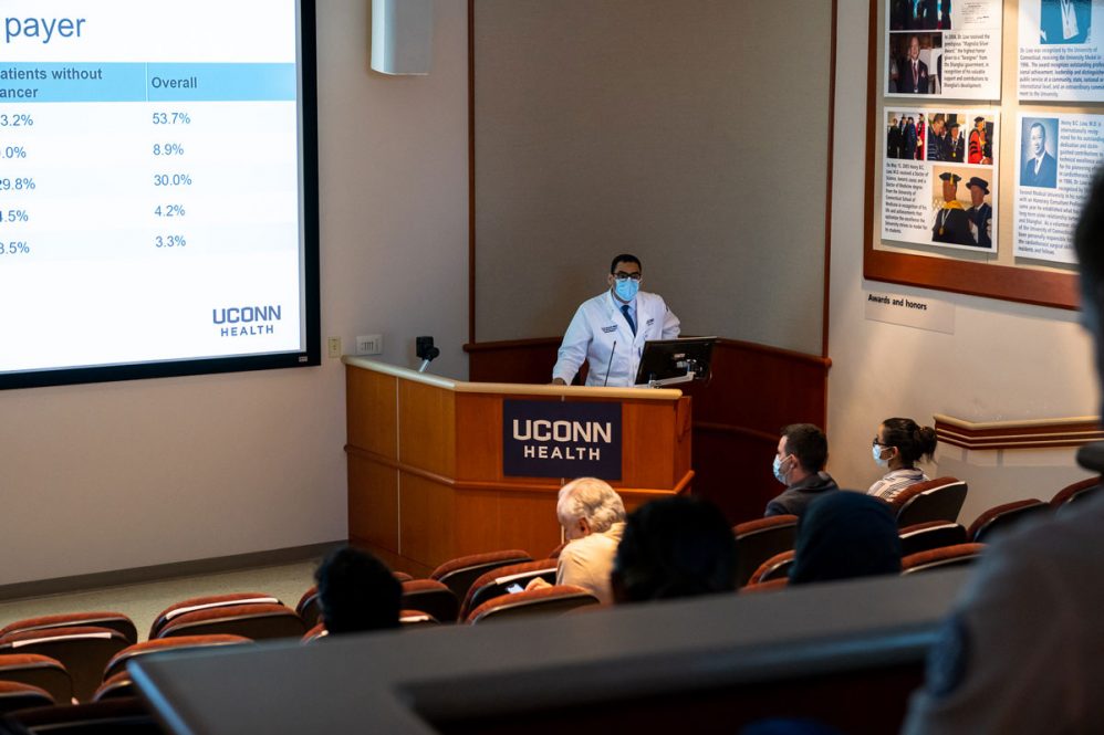 Dr. Khalid Shalaby in white coat presenting at podium
