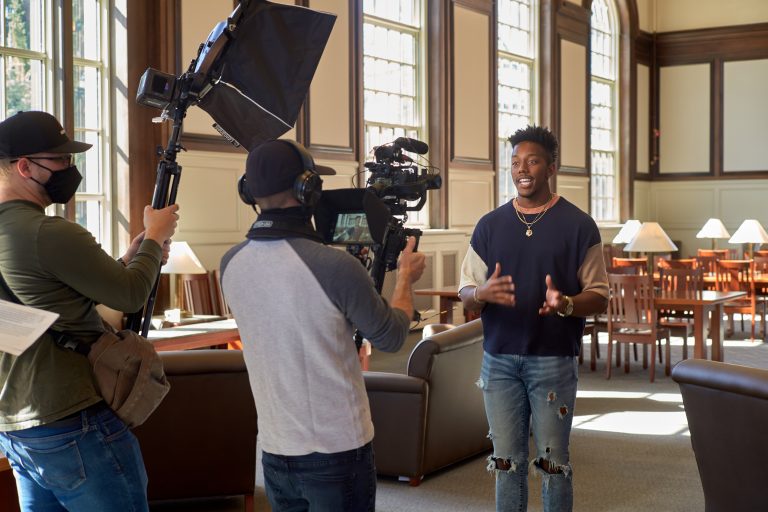 a student being interviewed by a tv crew in the North Reading Room of Wilbur Cross