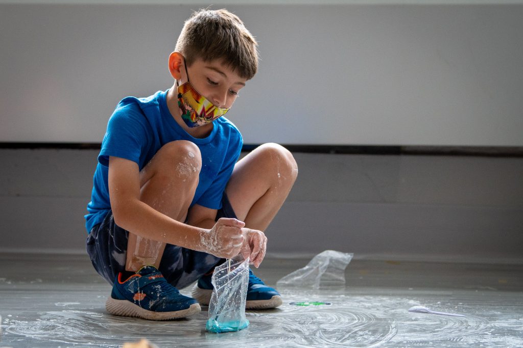 A boy squats to mix water and corn starch with blue food dye to make oobleck.