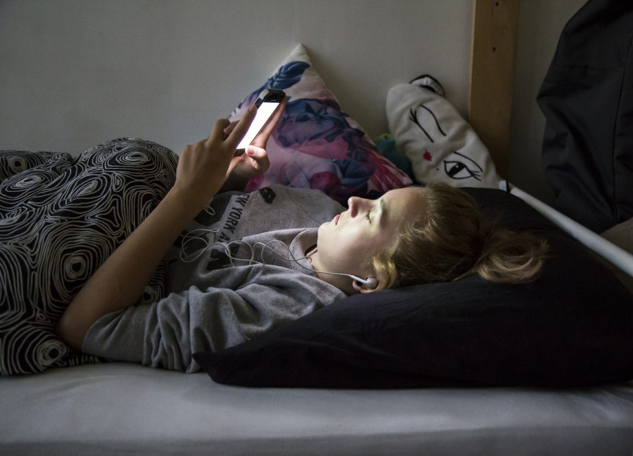 Teenager is looking mesmerized at her phone in bed in a dark bedroom
