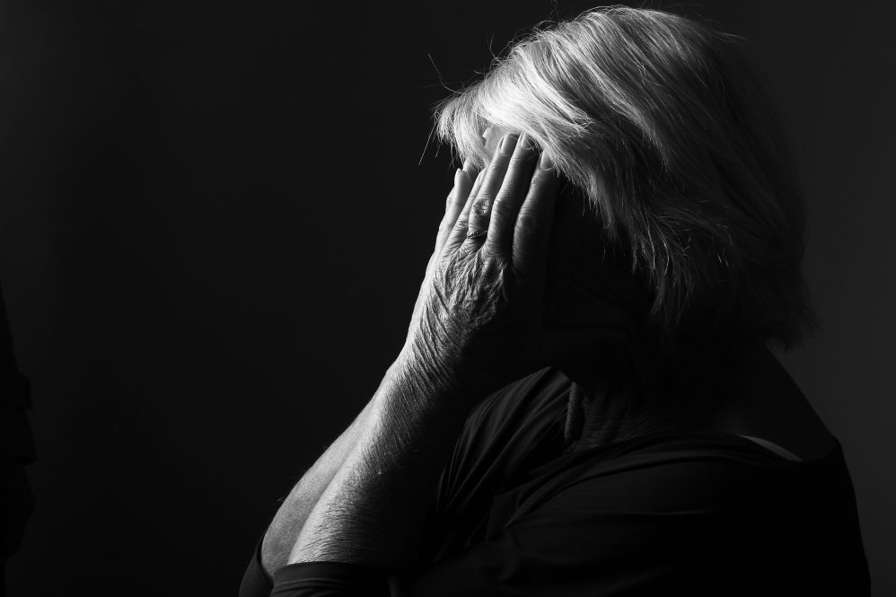 An older woman shields her face with her hands, shrouded in darkness, symbolizing depression. Research shows that ECT given to older adults as psychiatric inpatients is effective at preventing them from dying by suicide in the first months after release from the hospital.