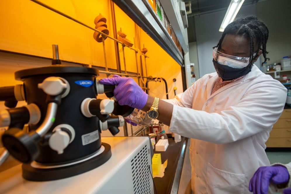 Nichali Bogues conducts an experiment wearing face masks and goggles in his lab.