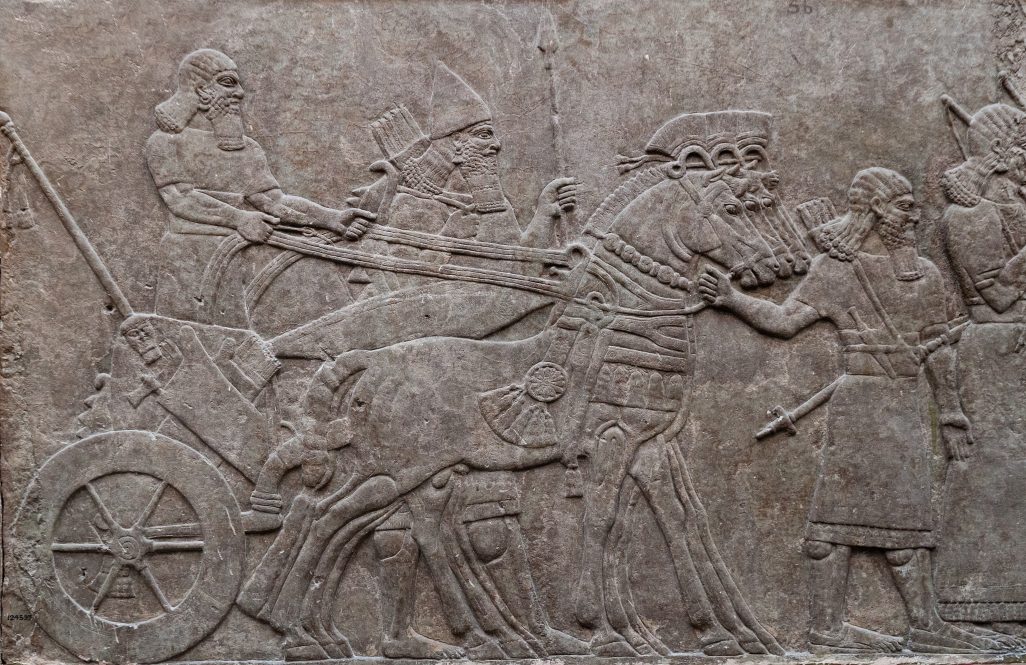 Relief of ancient assyrian warriors in a horse drawn chariot.