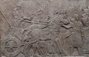 Relief of ancient assyrian warriors in a horse drawn chariot.