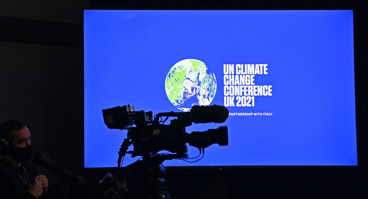 A television camera operator works in front of a COP26 logo displayed on a screen ahead of an event on the sidelines of the COP26 UN Climate Change Conference in Glasgow on November 9, 2021.
