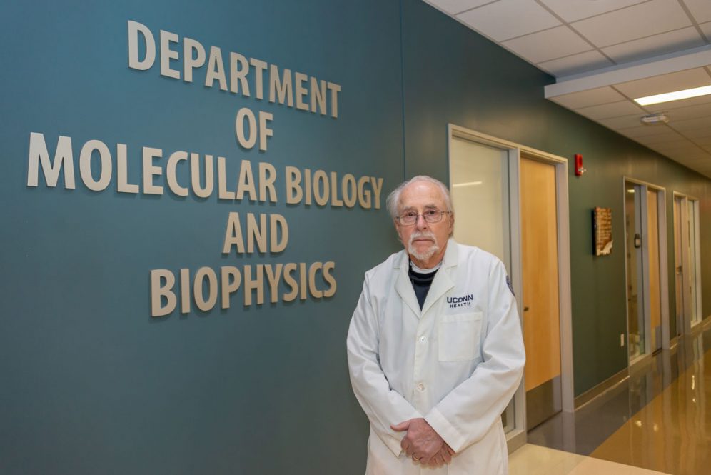 Peter Setlow portrait in front of Department of Molecular Biology and Biophysics sign