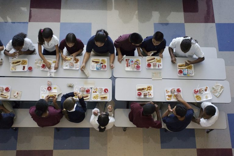 An overhead view of a school cafeteria table, where students are eating lunch.