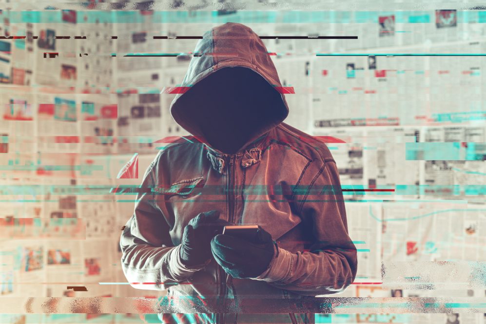 Hooded hacker person using smartphone in infodemic concept with digital glitch effect.
