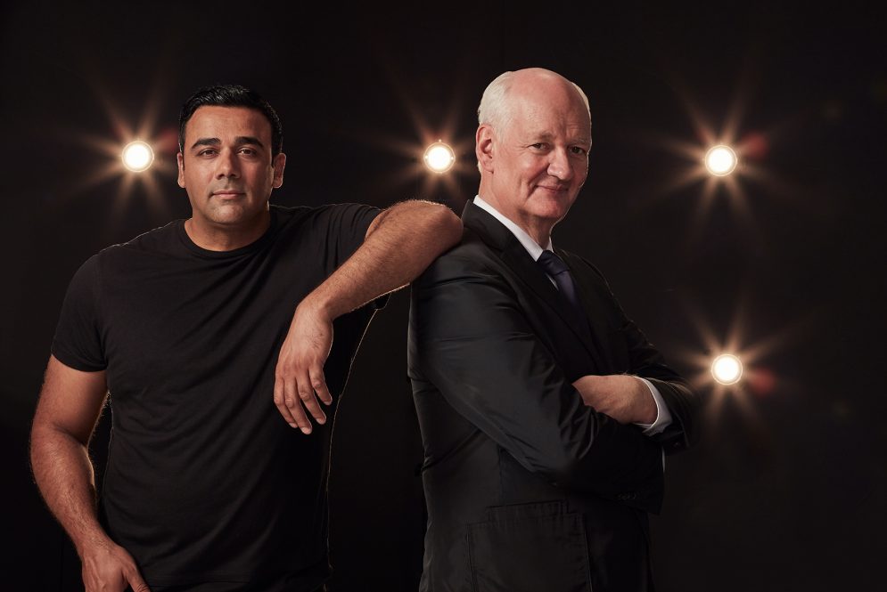 Hypnotist Asad Mecci and comedian Colin Mochrie, who are performing on Friday at Jorgensen, pose together in front of a dark backdrop illuminated by spotlights.