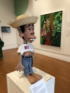 Table-top puppet Juan Bobo by Jose Alejandro Lopez is one of the first puppets on display in "Hecho en Puerto Rico: Four Generations of Puerto Rican Puppetry" at the Ballard Institute and Museum of Puppetry. On the right is an oil painting of Pura Belpre, a Puerto Rican puppeteer, librarian, and author.