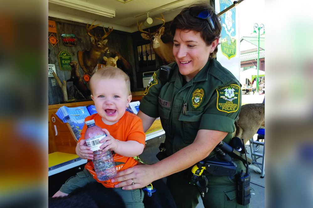 Elise Bouthillier, a UConn alumna, wears her state Department of Environmental Protection uniform as she lifts a small boy, wearing an orange shirt.