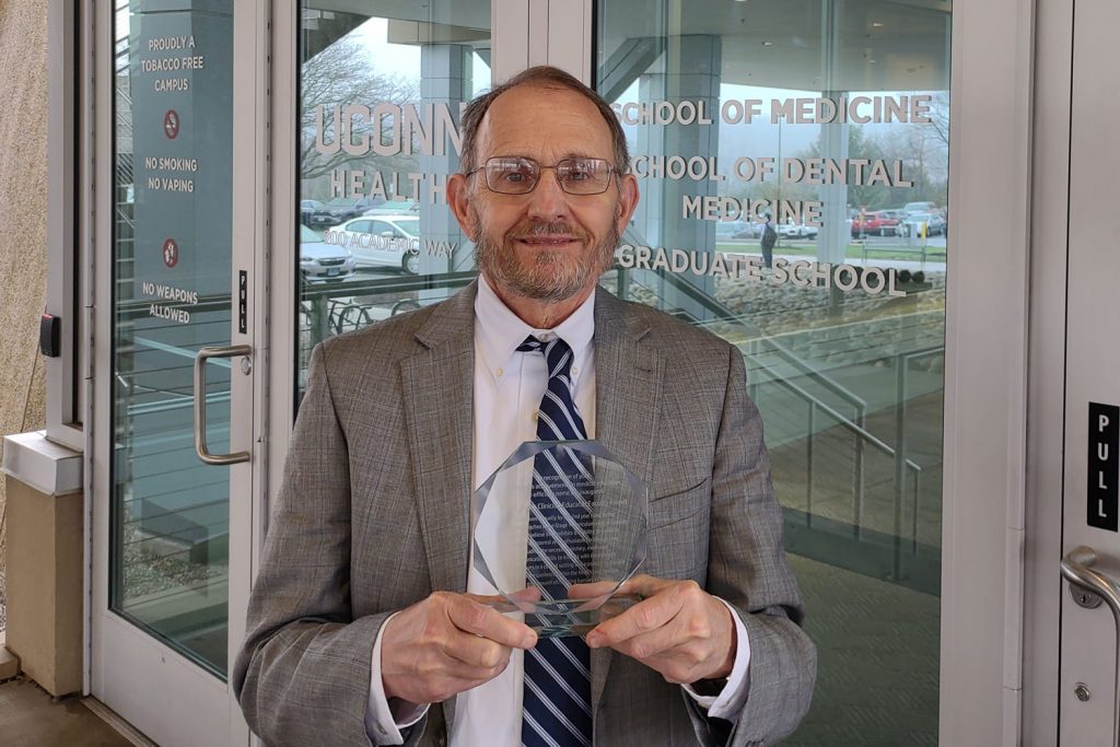 Dr. Dan Henry holding plaque outside academic entrance