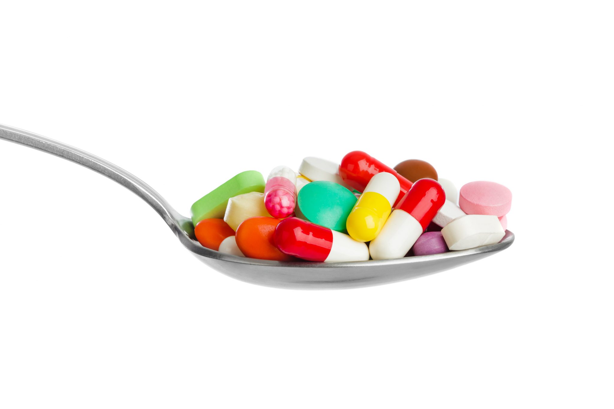Spoon with pills isolated on white background.