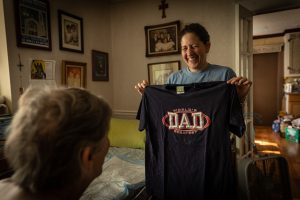 Leandra Manos smiles while showing her “Baba” his shirt for the day. Leandra converted her front room into a living space for her father, George, allowing him to easily access the kitchen and bathroom. She rents out the home’s second story to help her pay the bills. This is one image from Smith's photo essay, "A Daughter's Long Goodbye," which has won several awards this year.