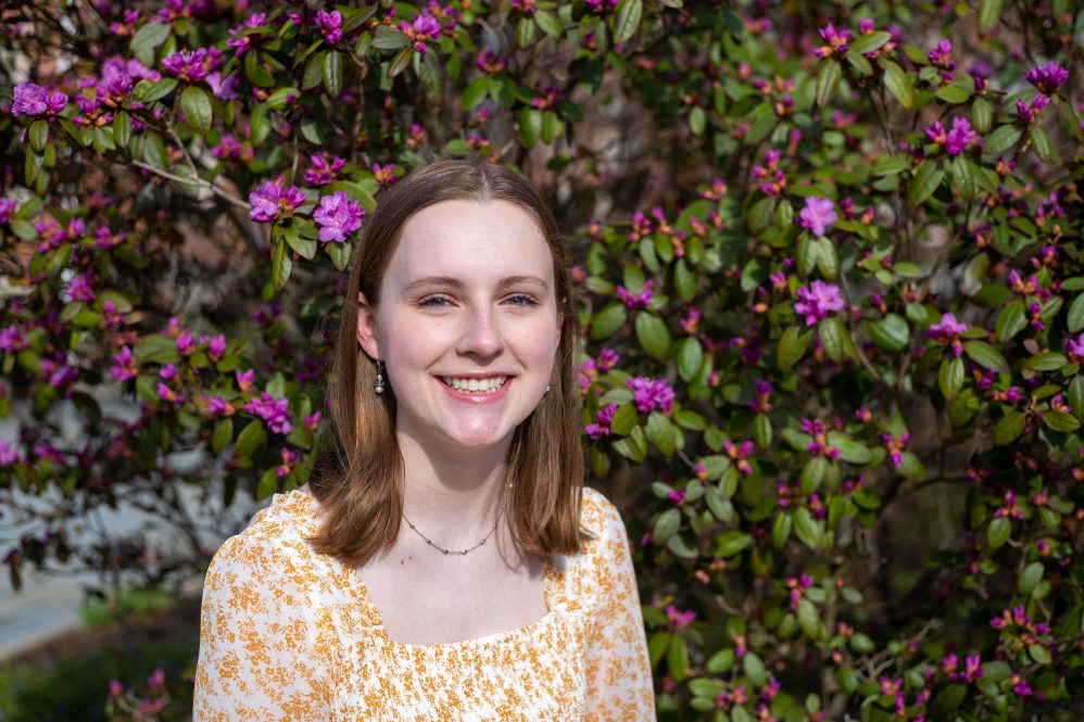 Katie Hooker, a Barry Goldwater scholarship recipient, in front of a flowering bush on campus