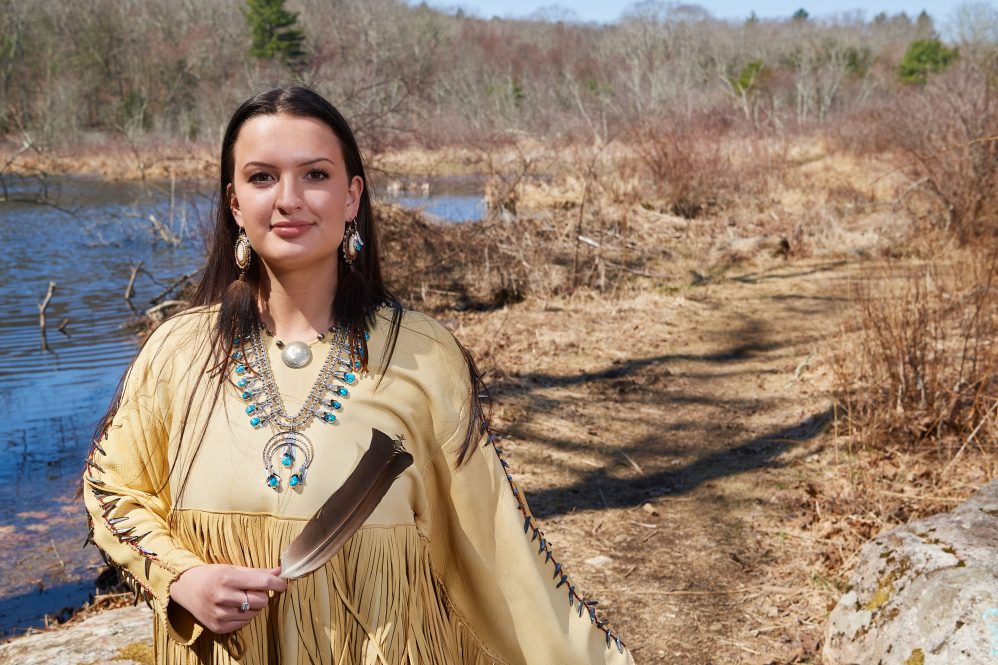 Sage Phillips '22 (CLAS) wears traditional Penobscot clothing while standing near wetlands in the Fenton tract of the UConn Forest