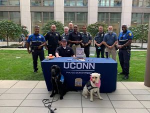 A group of UConn police officers - with two police dogs - pose around a table covered with a blue cloth.