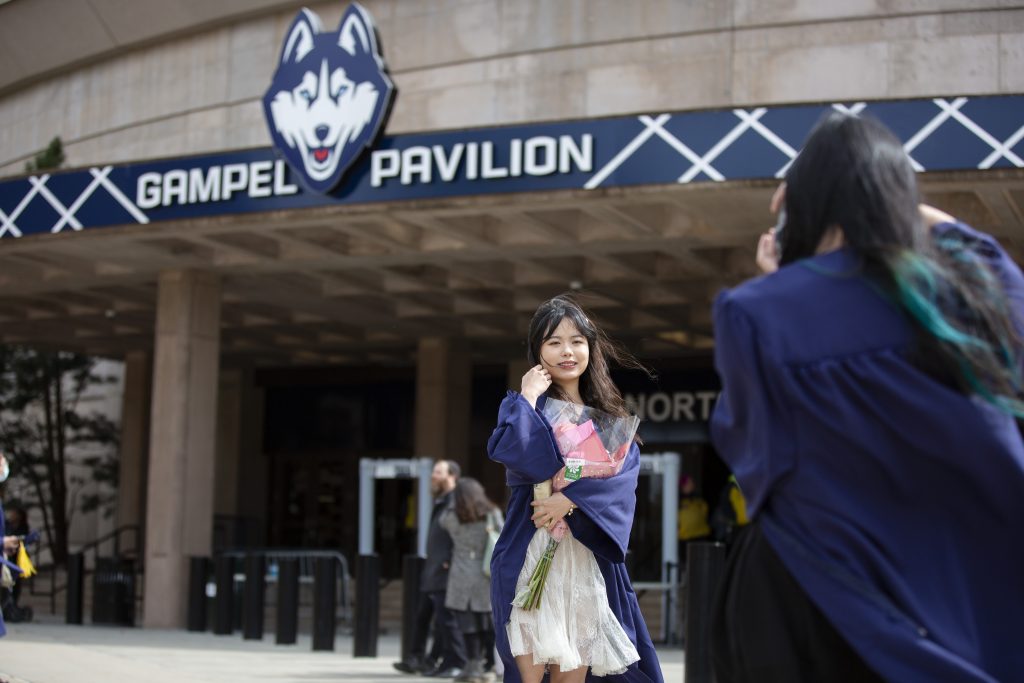 Graduate poses in front of Gampel Pavilion