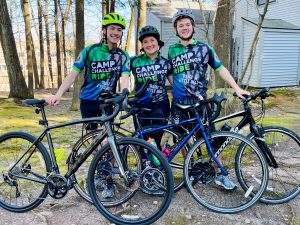 Three students in biking gear group portrait outdoors with bicycles