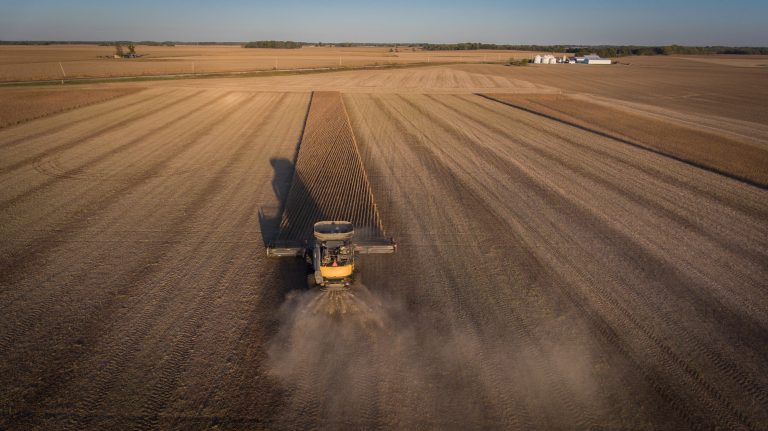 Aerial image of combine harvesting soybeans at sunset in a field in the Midwest United States.
