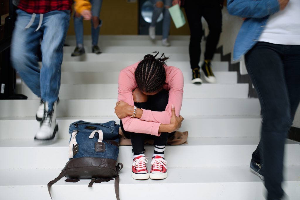 Depressed young student with face mask sitting on floor back at college or university.