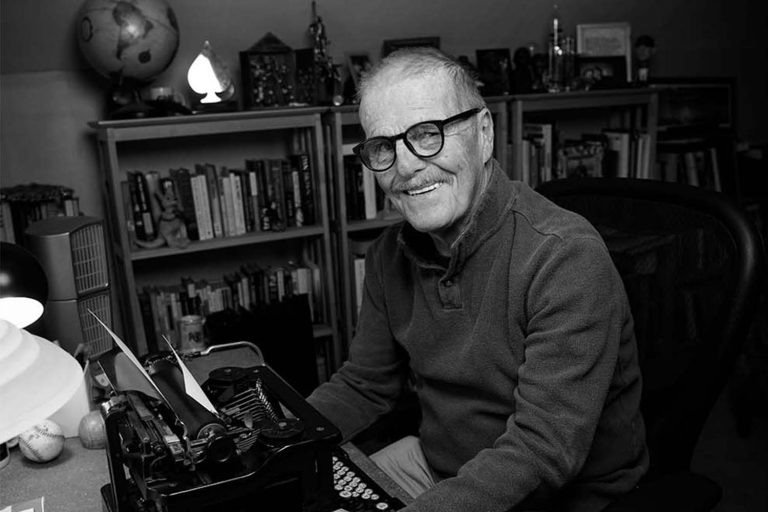 Black & white photo of sportswriter Leigh Montville sitting down in front of a typewriter