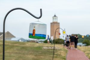 Walkers on the trail along the coast at UConn Avery Point walk past painted candle holders created by artist Beth Reitmeyer when she arrived on campus during the Open Air Art Exhibitionâ€™s opening reception on July 14, 2022. (Sydney Herdle/UConn Photo).