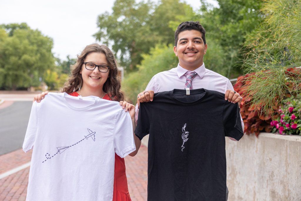 UConn students Audrey Larson, left, and Angel Velasquez pose for a photo on campus on Aug. 17, 2022 with shirts from the apparel company they run together that hopes to partner artists with charities.