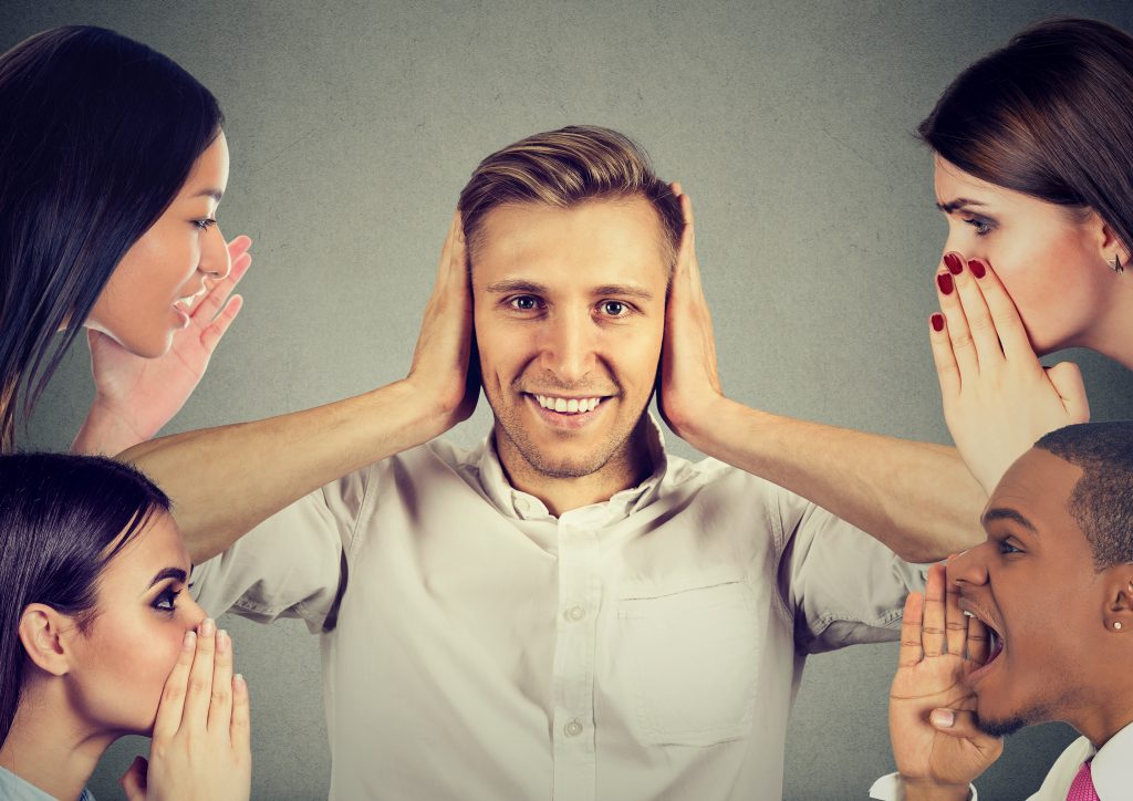 Man and women whispering a secret latest gossip to a happy young man who covers ears and ignoring all surrounding noise.