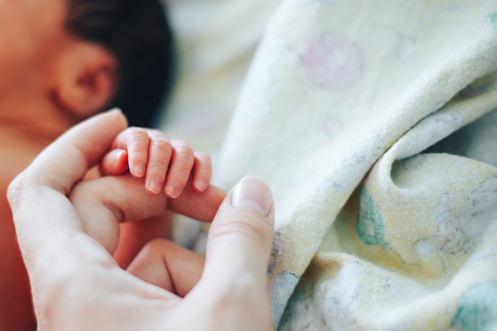 Close-up shot of baby's little cute hand reaching for mother's loving hand. While holding her finger she caresses his hand.