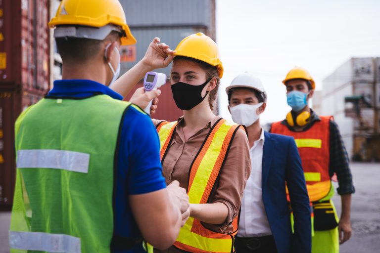 Worker scanning fever temperature with digital thermometer to construction site staff wearing hygiene face mask protect from Coronavirus or COVID-19.