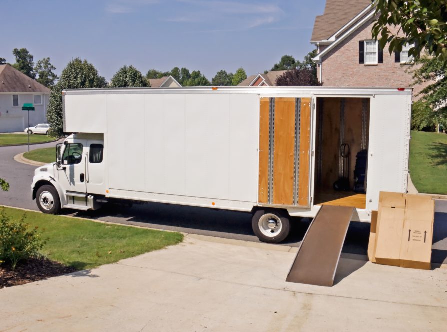 A moving van parked at the driveway of a house, with a ramp leading into the open trailer.